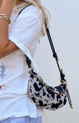 a girl wears a black cow print shoulder bag over her shoulder and a white top