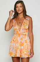 Model is pictured holding a cocktail, wearing an orange, floral, mini dress. The dress has an elasticated waist and deep cut V neckline. 