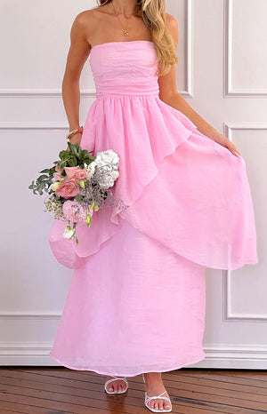 a woman wears a pink strapless maxi dress and white heels holding a bouquet of flowers