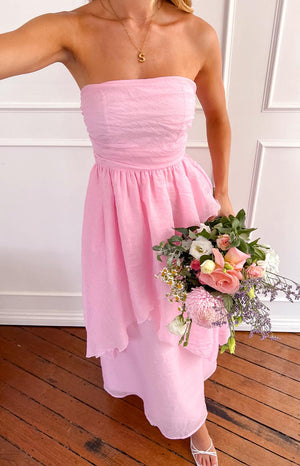 a woman holding a bouquet of flowers poses in a pink strapless maxi dress and white heels