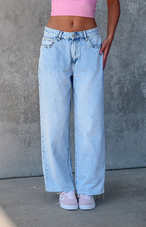 Lower body close up of girl in vintage blue denim jeans standing in front of a grey wall.